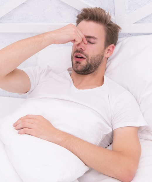 Man pinching bridge of nose in bed needing insomnia treatment in McKinney