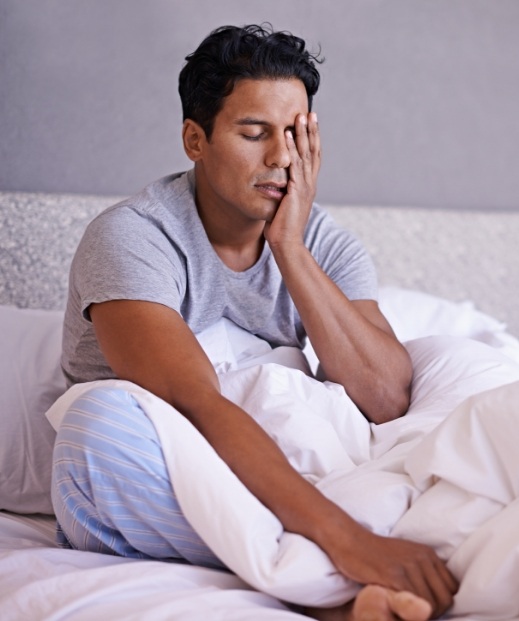 Man with obstructive sleep apnea in McKinney sitting up in bed rubbing his eyes