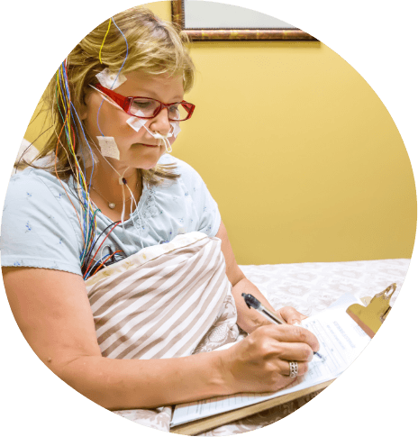 Woman writing on clipboard while hooked up to sleep testing sensors